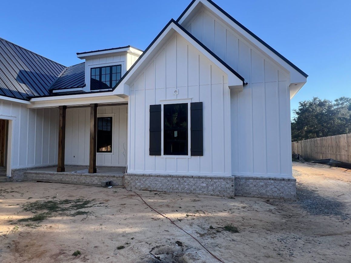 White farmhouse under construction, black roof, wooden porch supports, black windows.