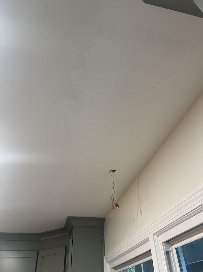 Ceiling with exposed wires hanging down, near a window and a cabinet.