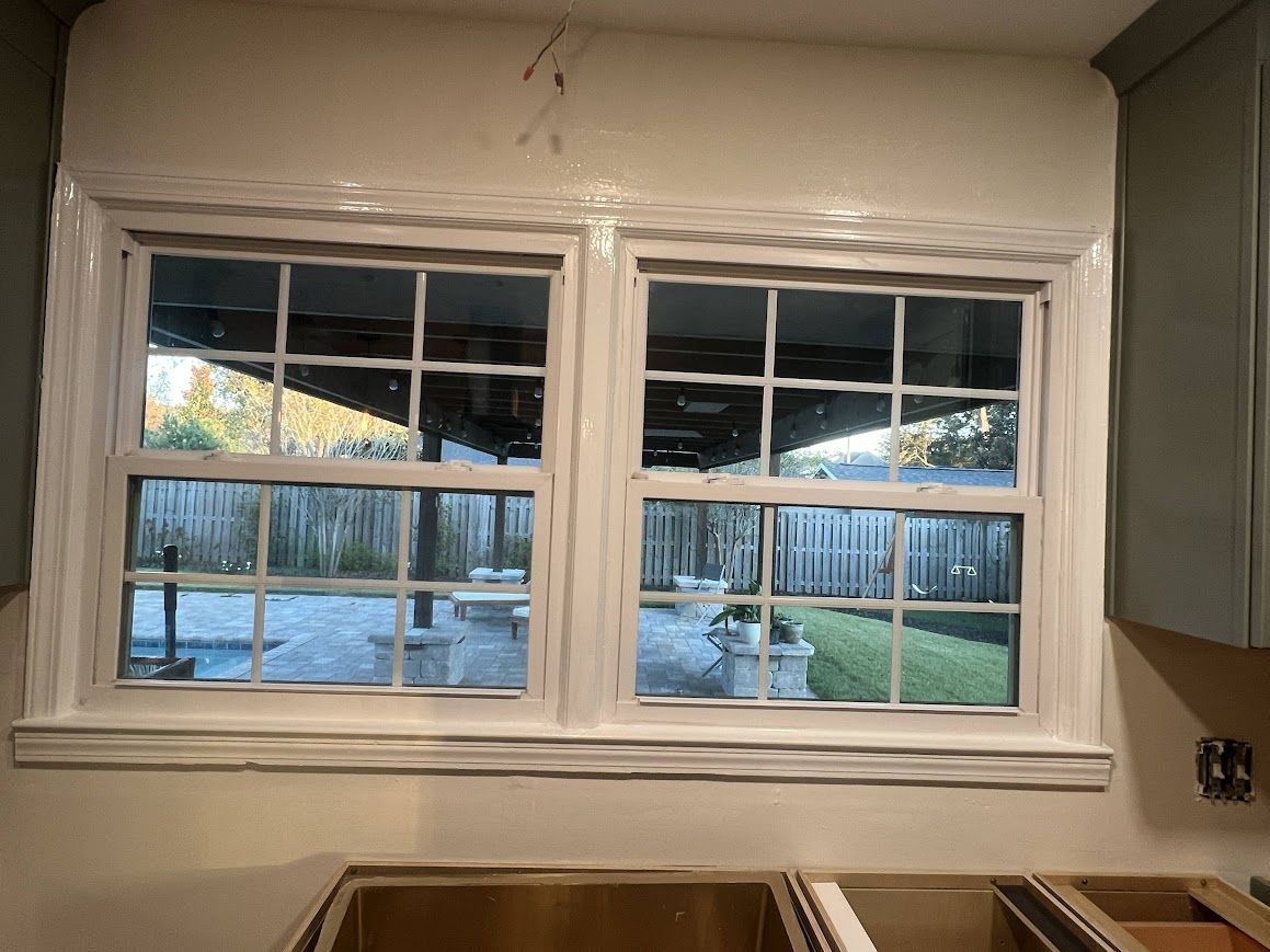 Two white-framed kitchen windows overlooking a backyard. Cabinets below are unfinished.