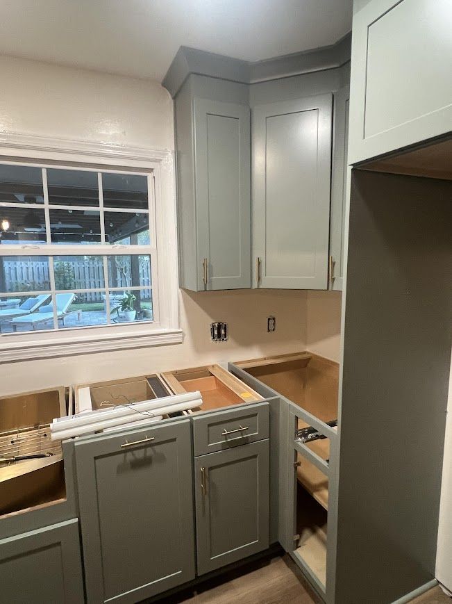 Kitchen under construction with light gray cabinets, unfinished counters, and a window.