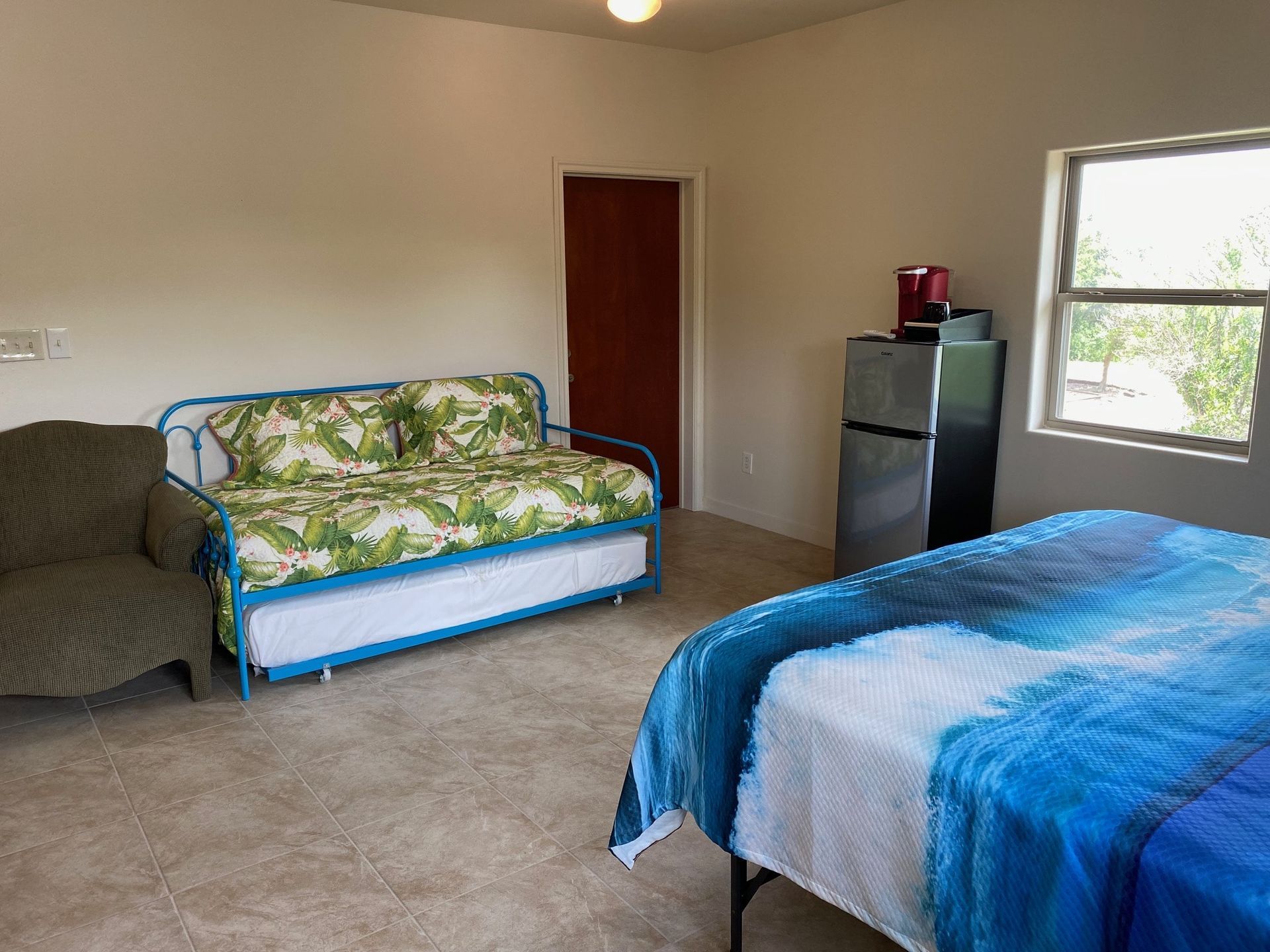 A bedroom with a bed , couch , chair and refrigerator.
