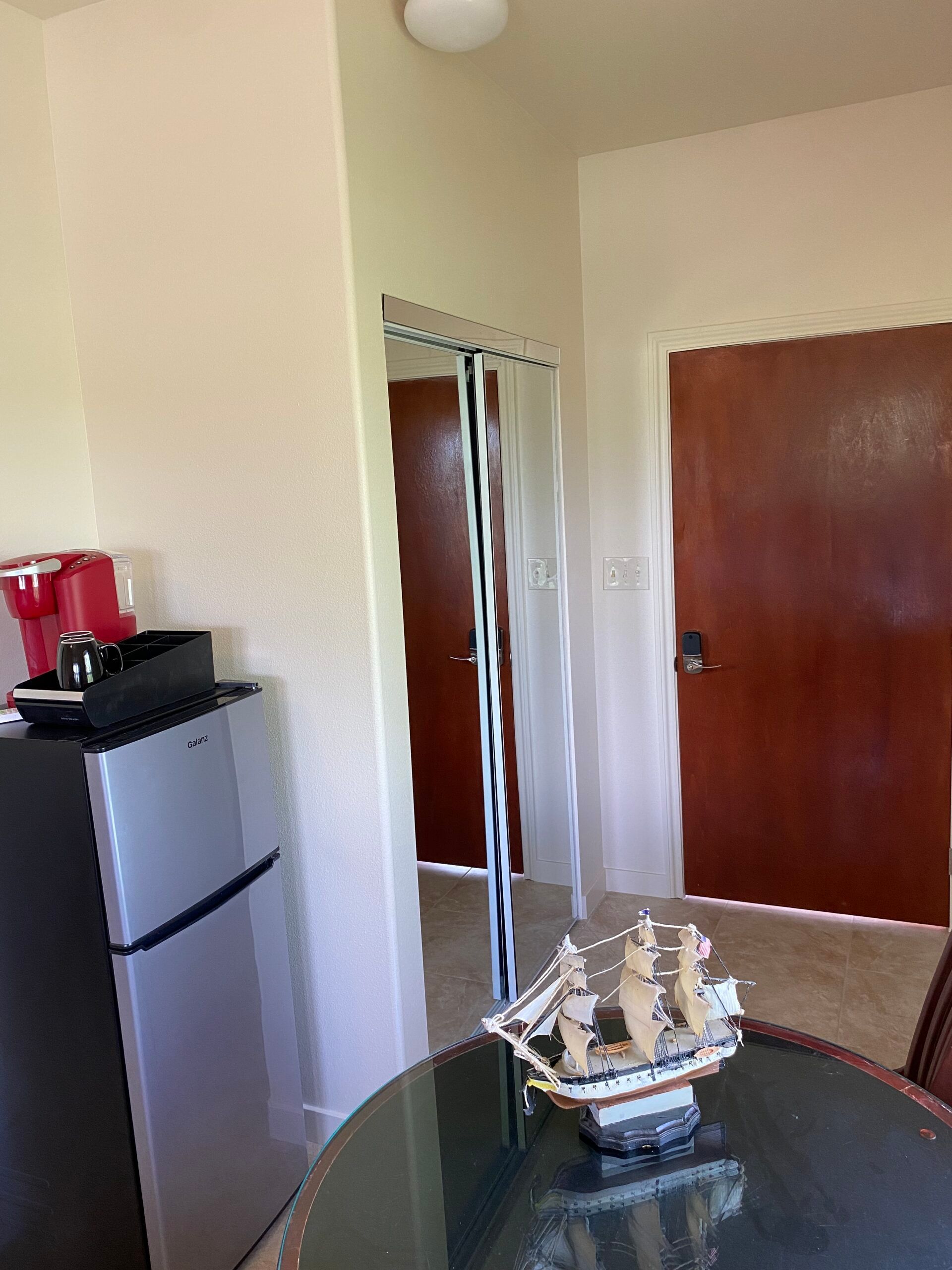 A room with a table , refrigerator , and a model ship on it.