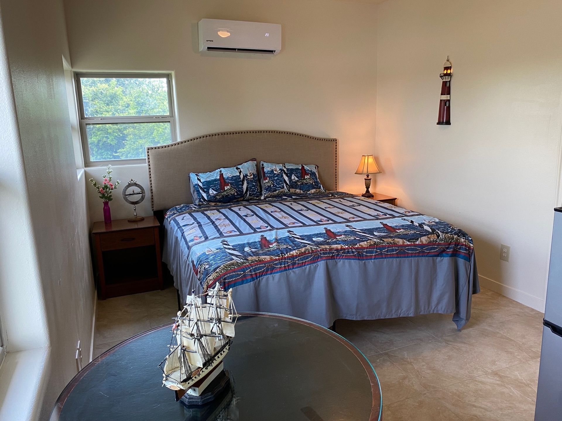 A bedroom with a bed , nightstand , table and window.