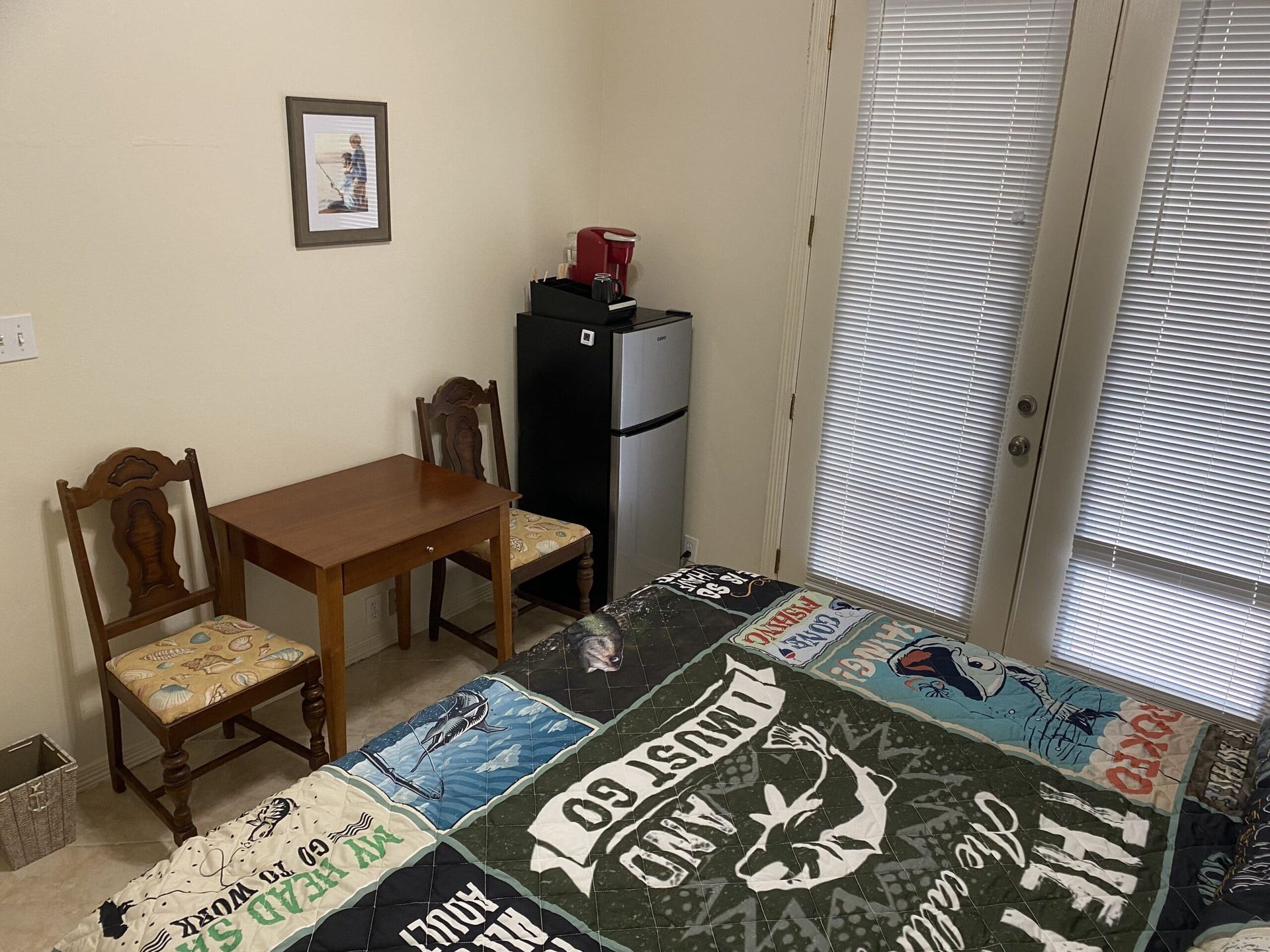 A bedroom with a bed , table , chairs and a refrigerator.