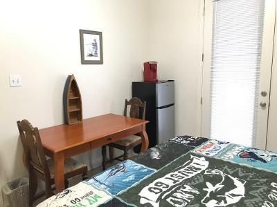 A bedroom with a bed , desk , chair and refrigerator.