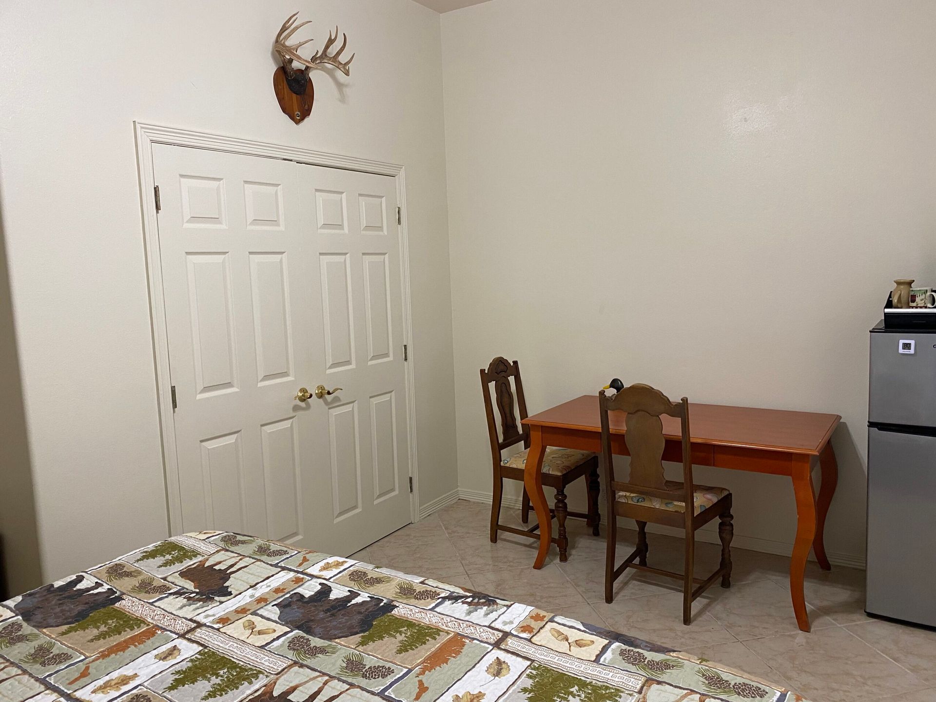 A bedroom with a bed , table , chairs and a refrigerator.