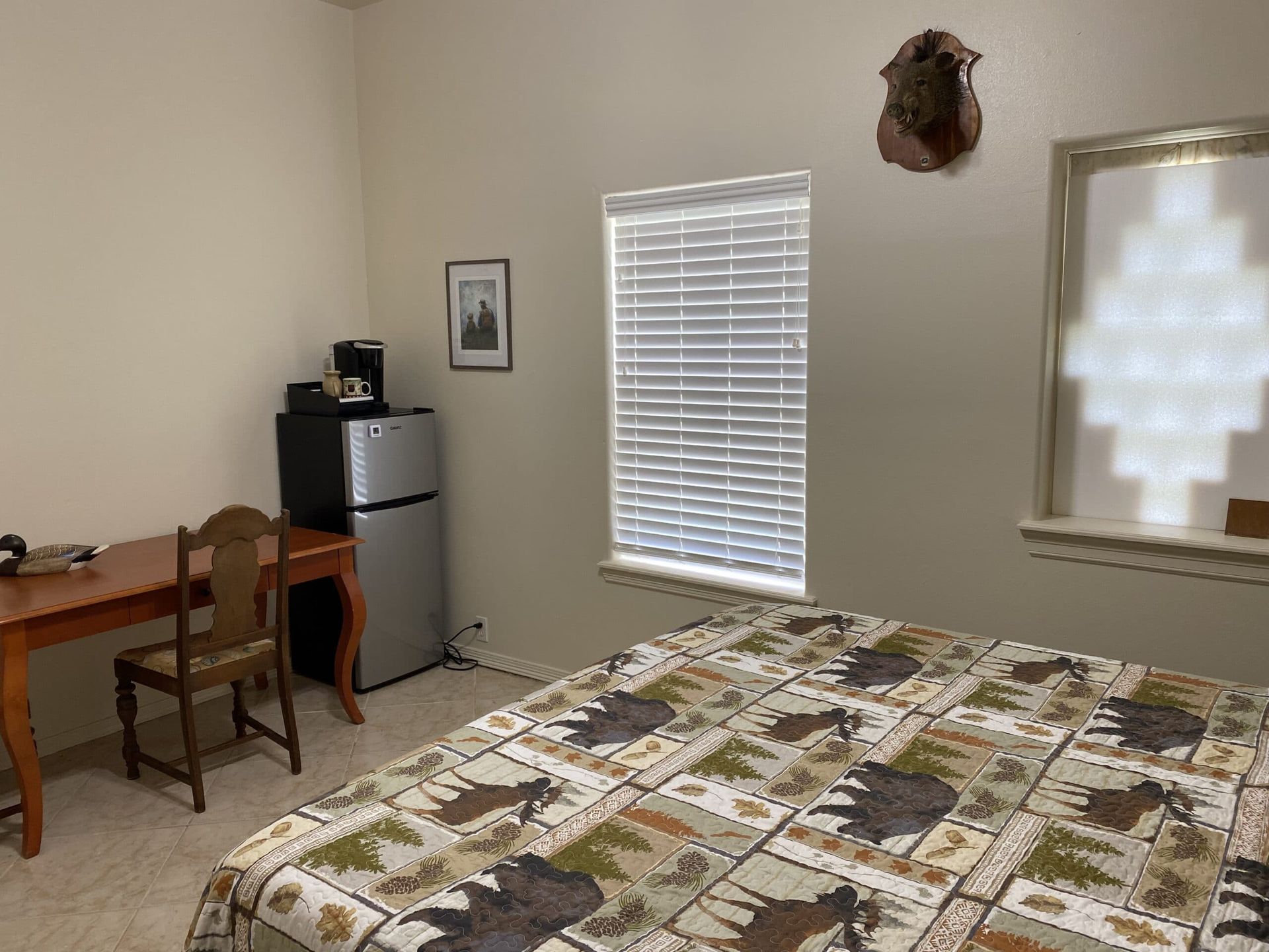 A bedroom with a bed , desk , chair and refrigerator.