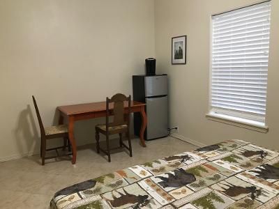A bedroom with a bed , desk , chair and refrigerator.