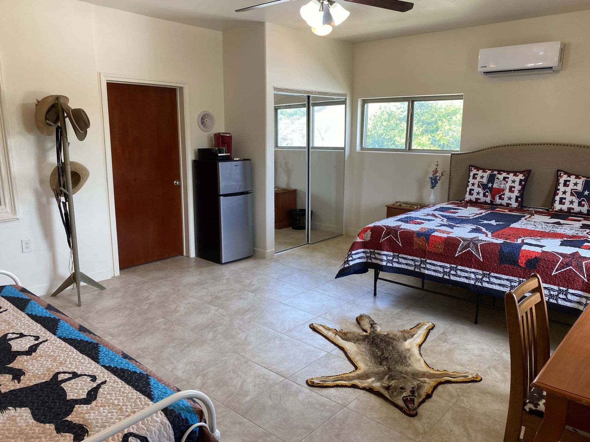 A bedroom with a bed , a rug , a refrigerator and a ceiling fan.