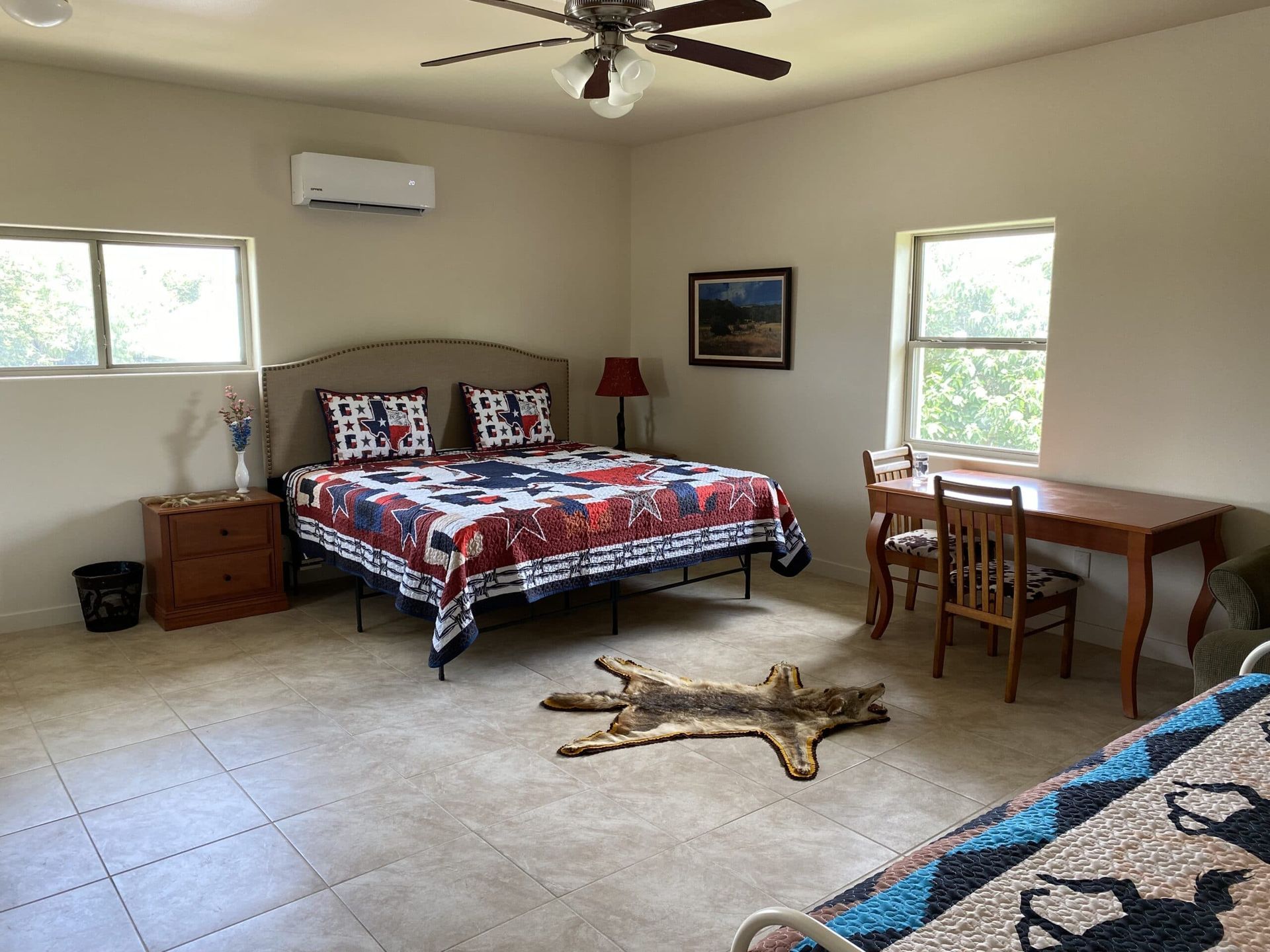 A bedroom with a bed , desk , chairs and a ceiling fan.