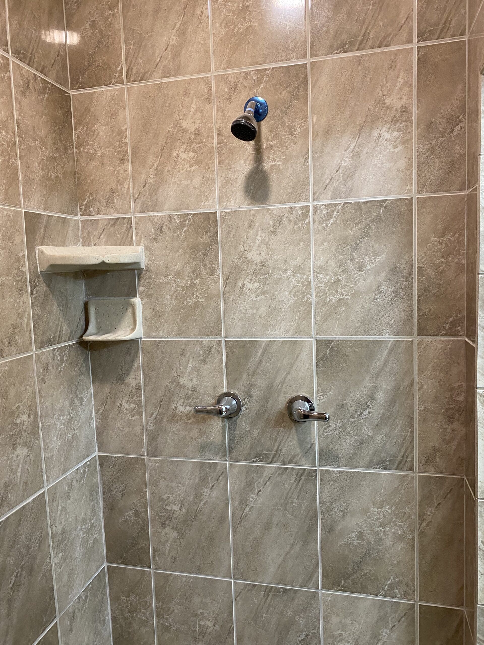 A shower with two shower heads and a soap dish on the wall.