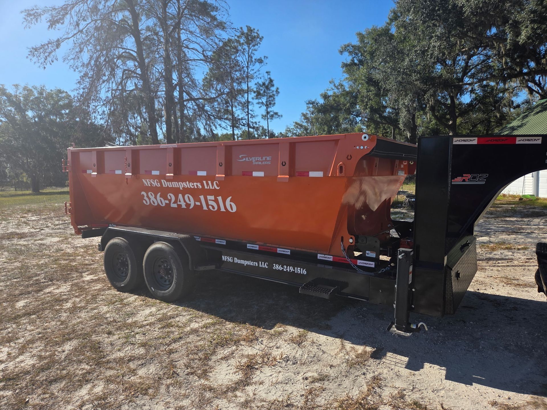 Orange dumpster trailer in a rural setting with the company's phone number on the side.