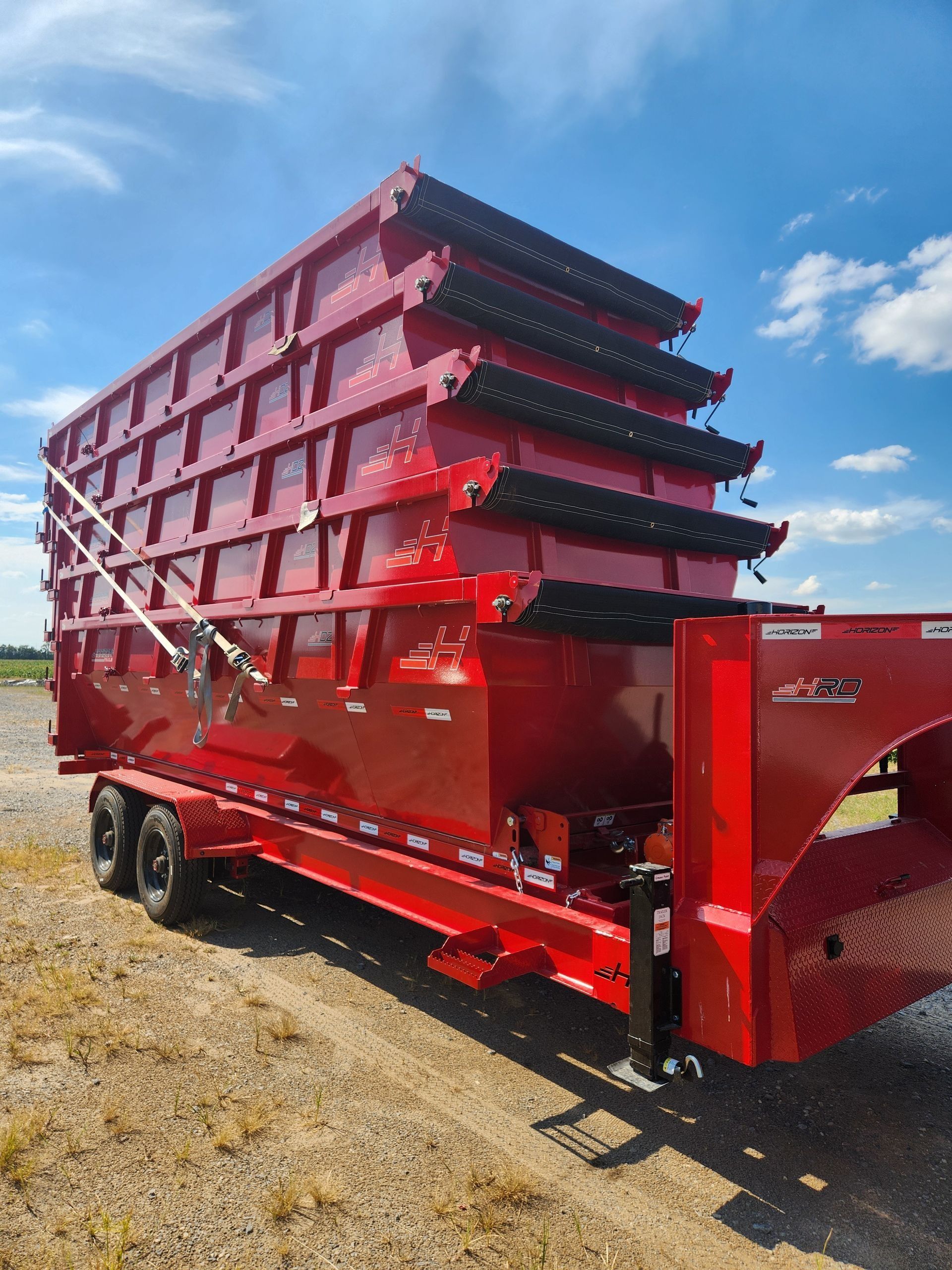 Red commercial trailer with stacked sections on a gravel road against a blue sky.