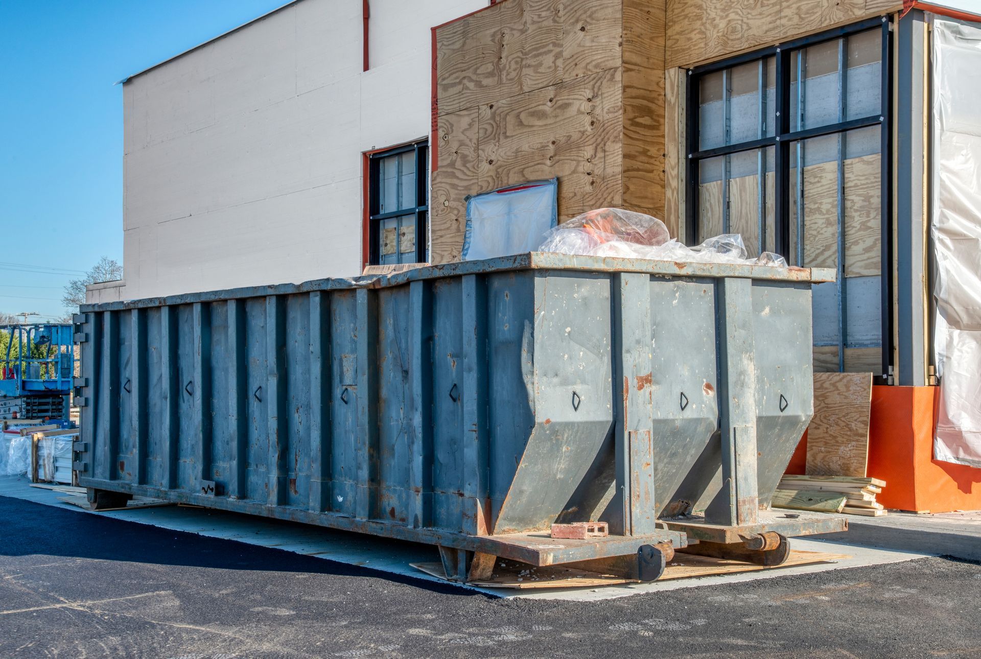 Large, gray construction dumpster outside building undergoing renovation.
