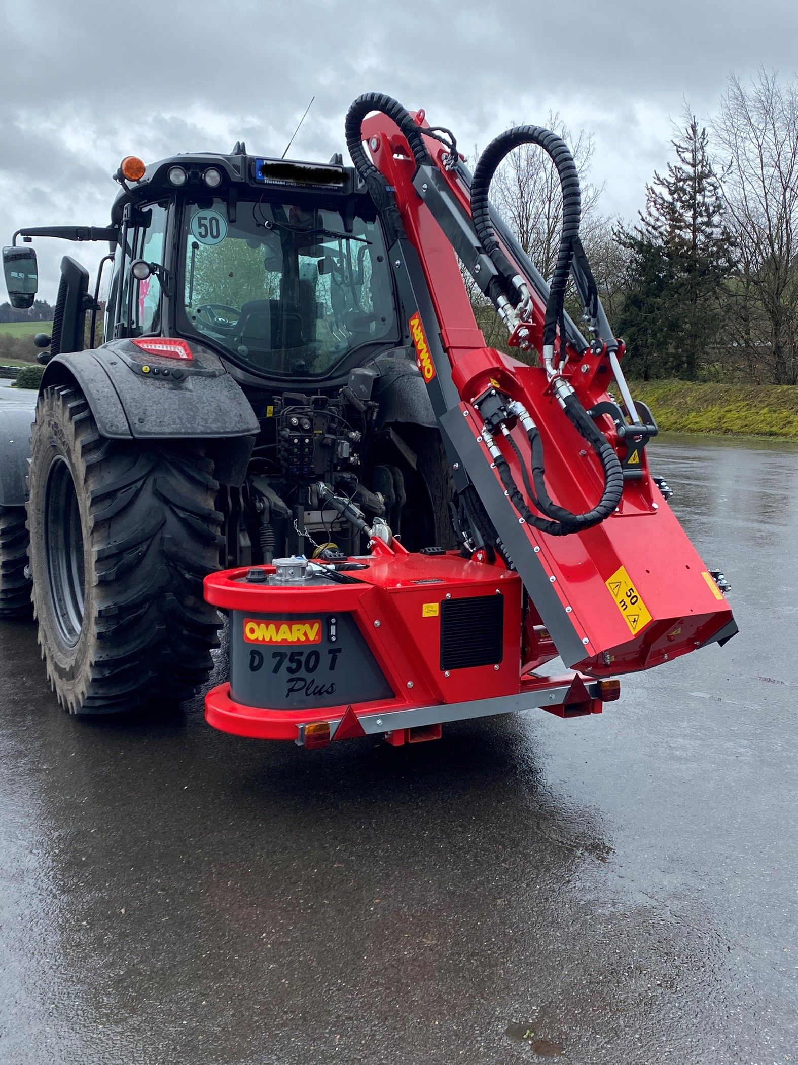 Ein Traktor mit einer daran befestigten Maschine mäht einen grasbewachsenen Hang.