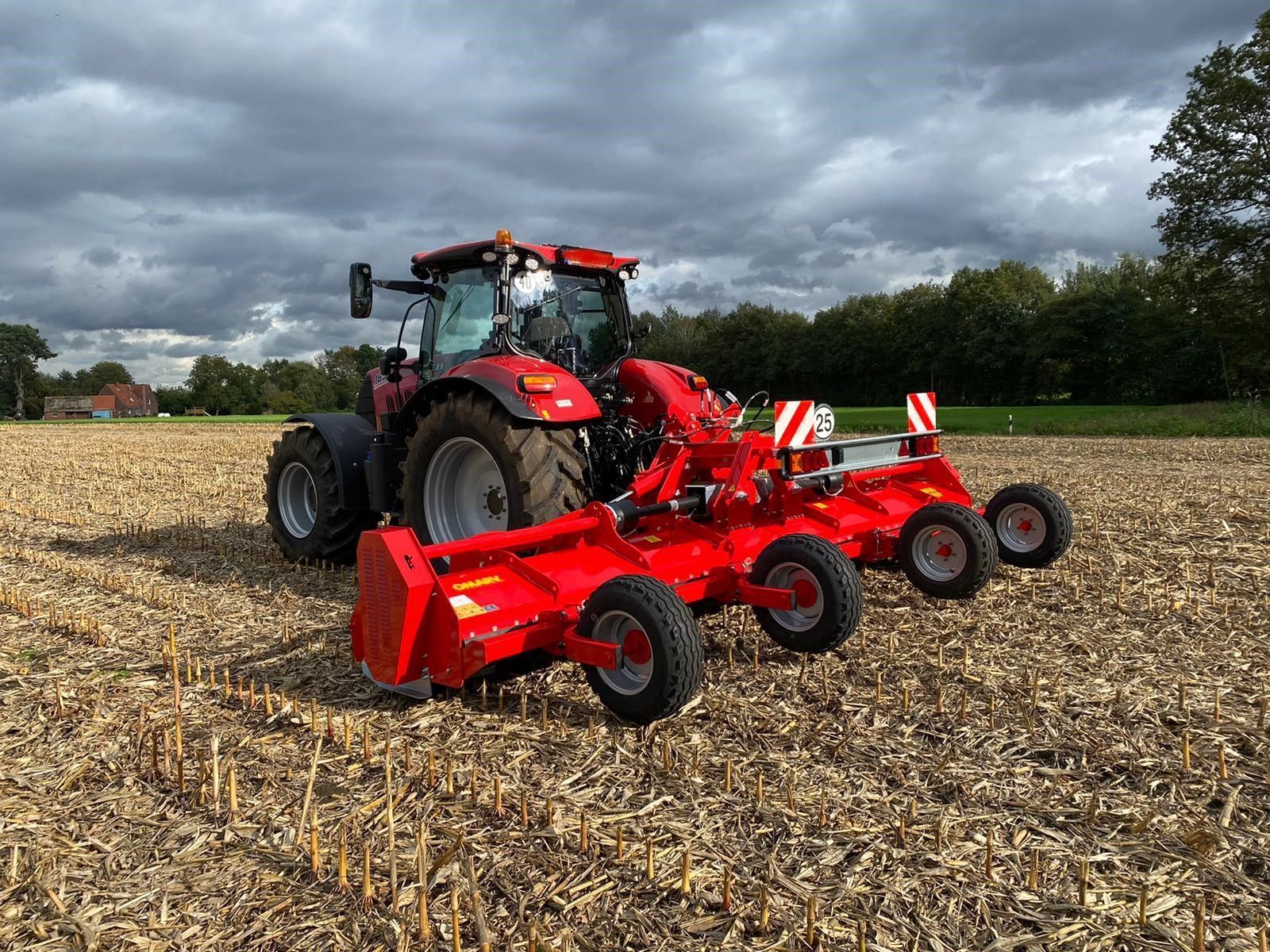 Ein roter Traktor fährt durch ein Feld mit trockenem Gras.
