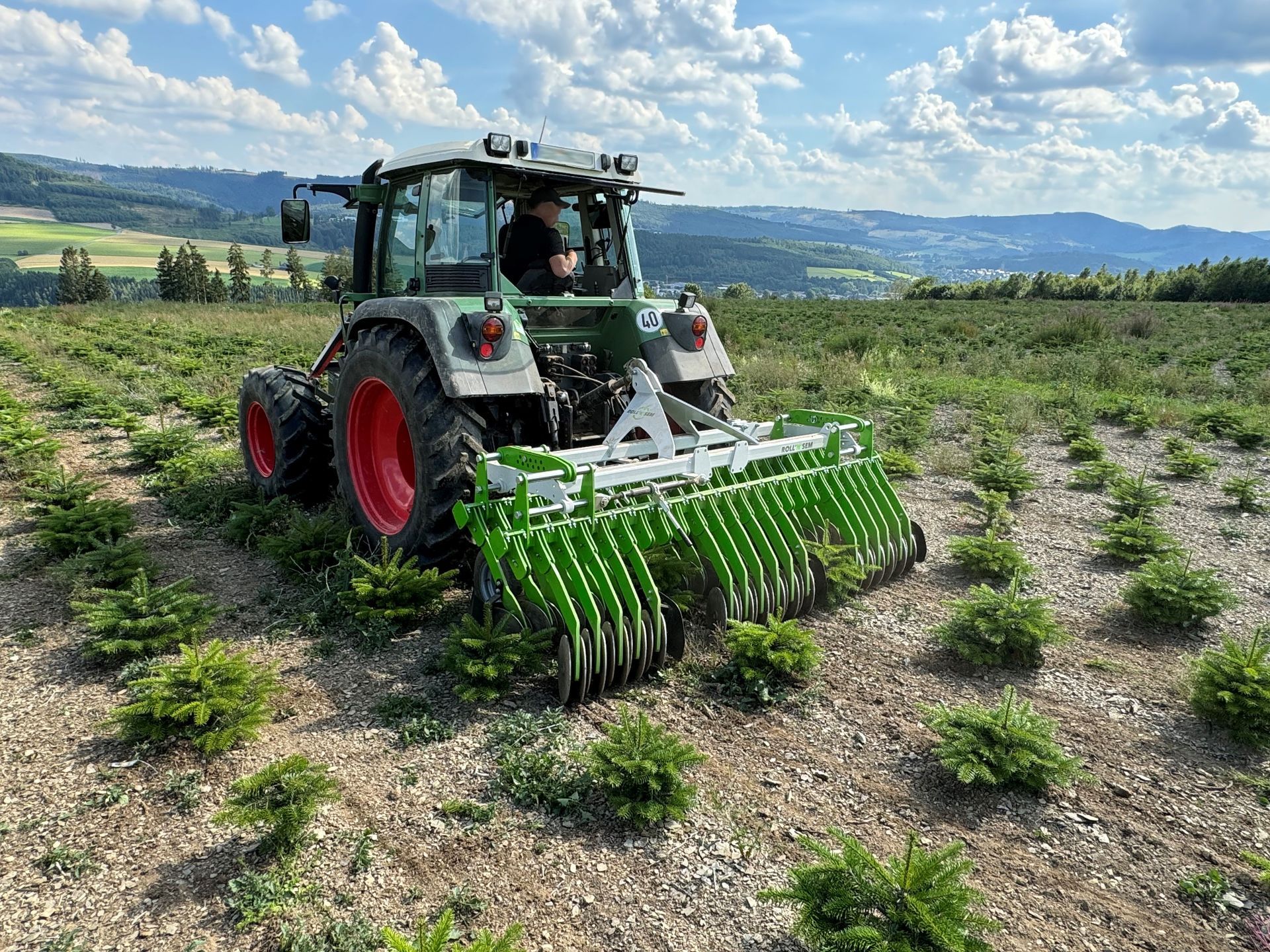 Ein Mann fährt mit einem Traktor durch ein Feld mit Bäumen.