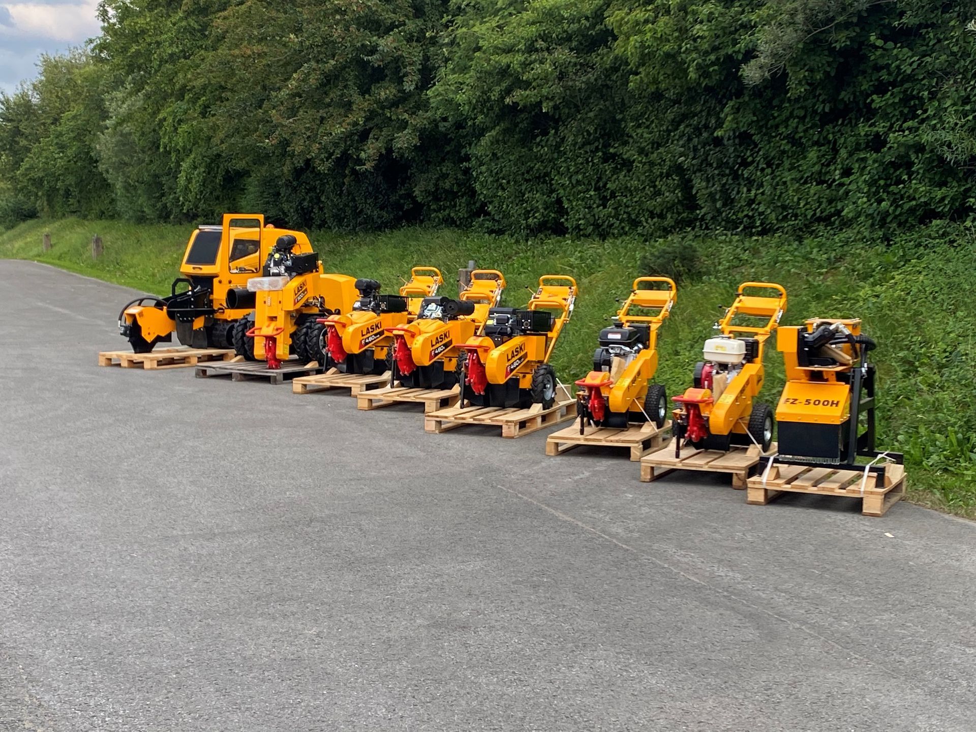 Eine Reihe gelber Rasenmäher steht auf Paletten am Straßenrand.