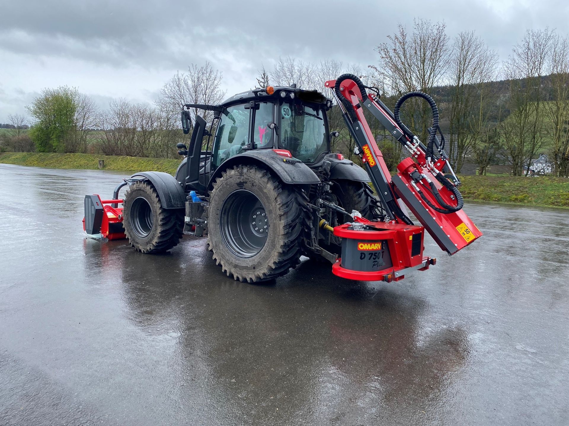 Ein rot-schwarzer Traktor steht am Straßenrand.