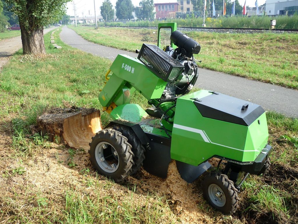 Ein grüner Traktor zerkleinert den Baumstumpf eines Baumes auf einem Feld.