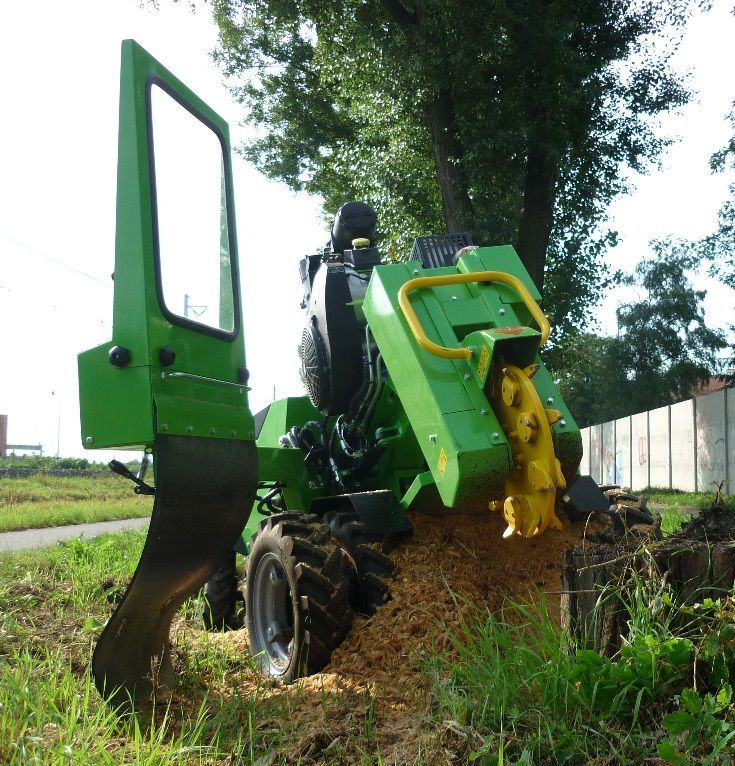 Ein grüner Traktor fräst den Stumpf eines Baumes auf einem Feld ab