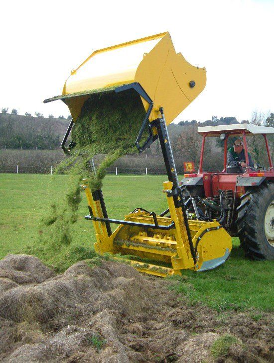 Ein Mann fährt einen Traktor mit einem gelben Eimer voller Gras