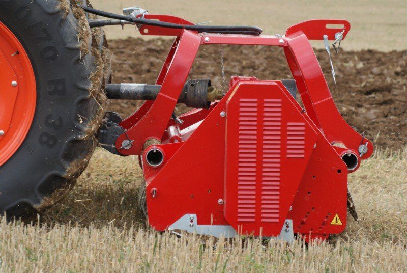 Eine rote Maschine steht neben einem Traktor auf einem Feld.