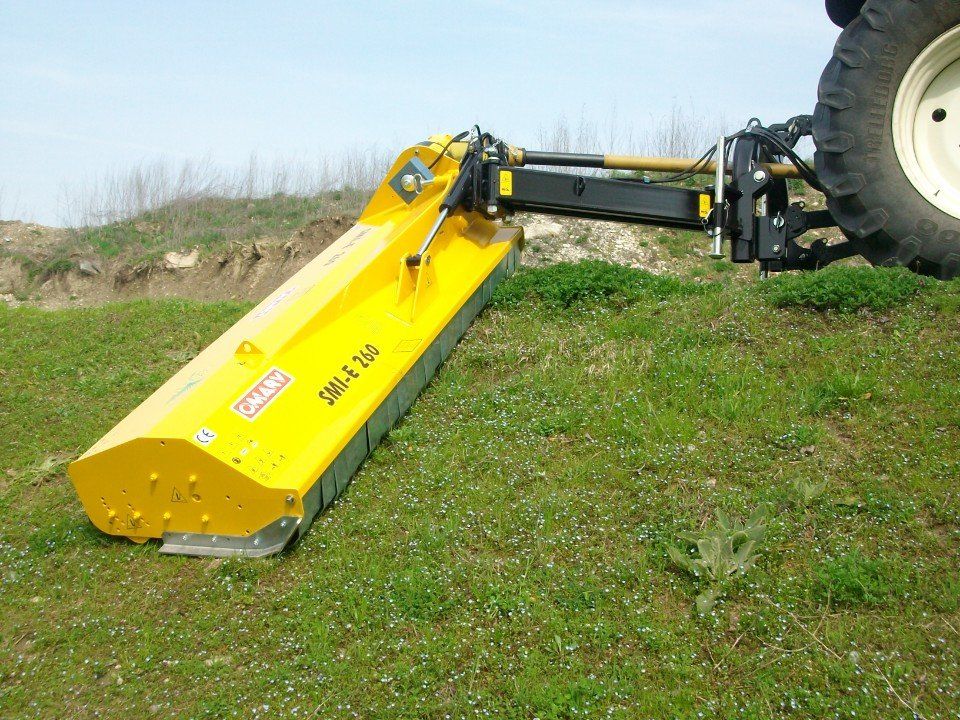 Auf einer Wiese ist ein gelber Rasenmäher an einen Traktor angehängt.