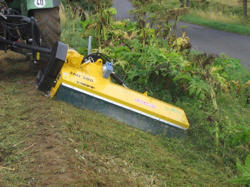 Ein gelber Traktor schneidet Gras neben einer Straße.