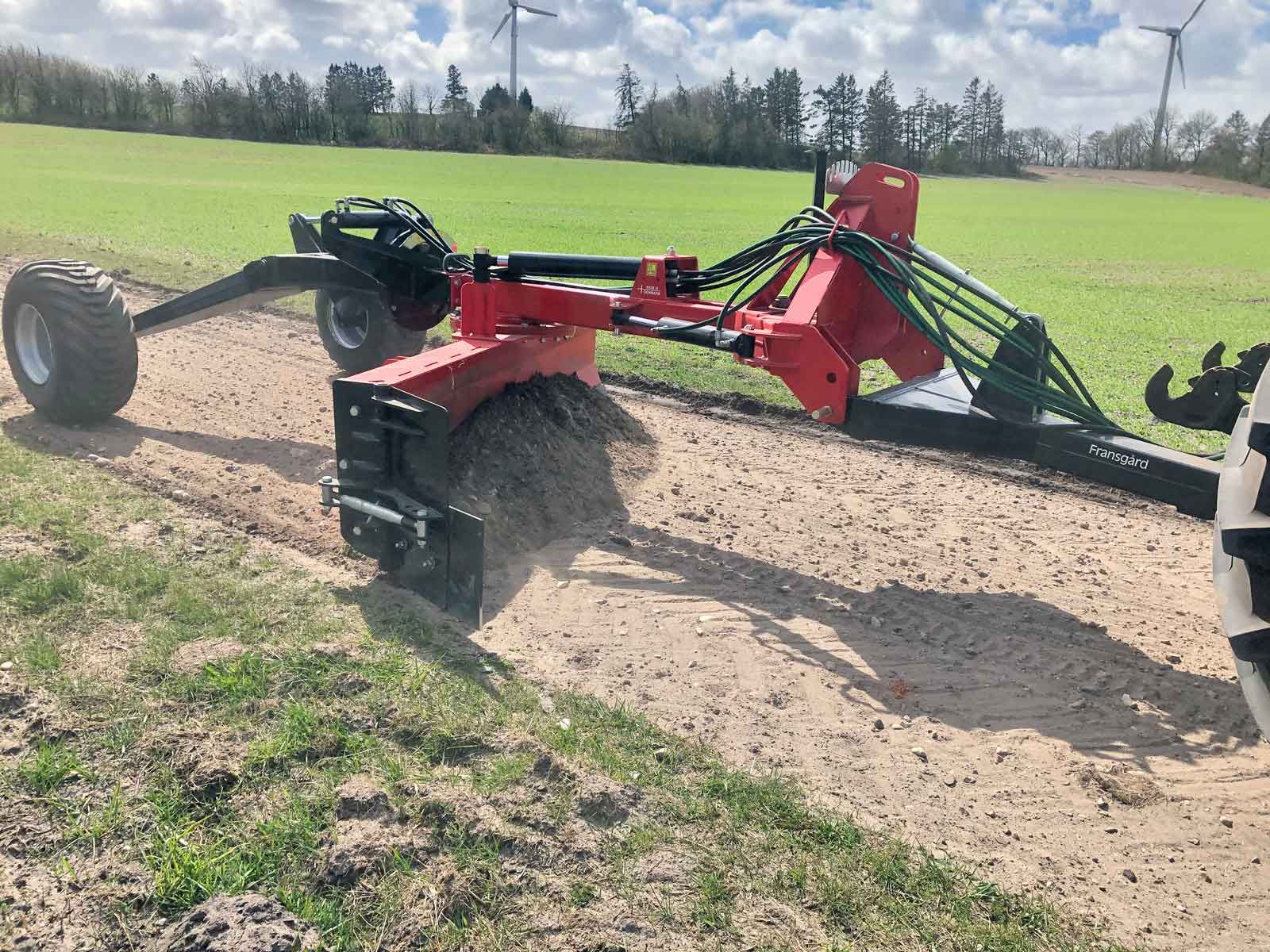 Eine rot-schwarze Maschine steht auf einem Feld auf einer unbefestigten Straße.