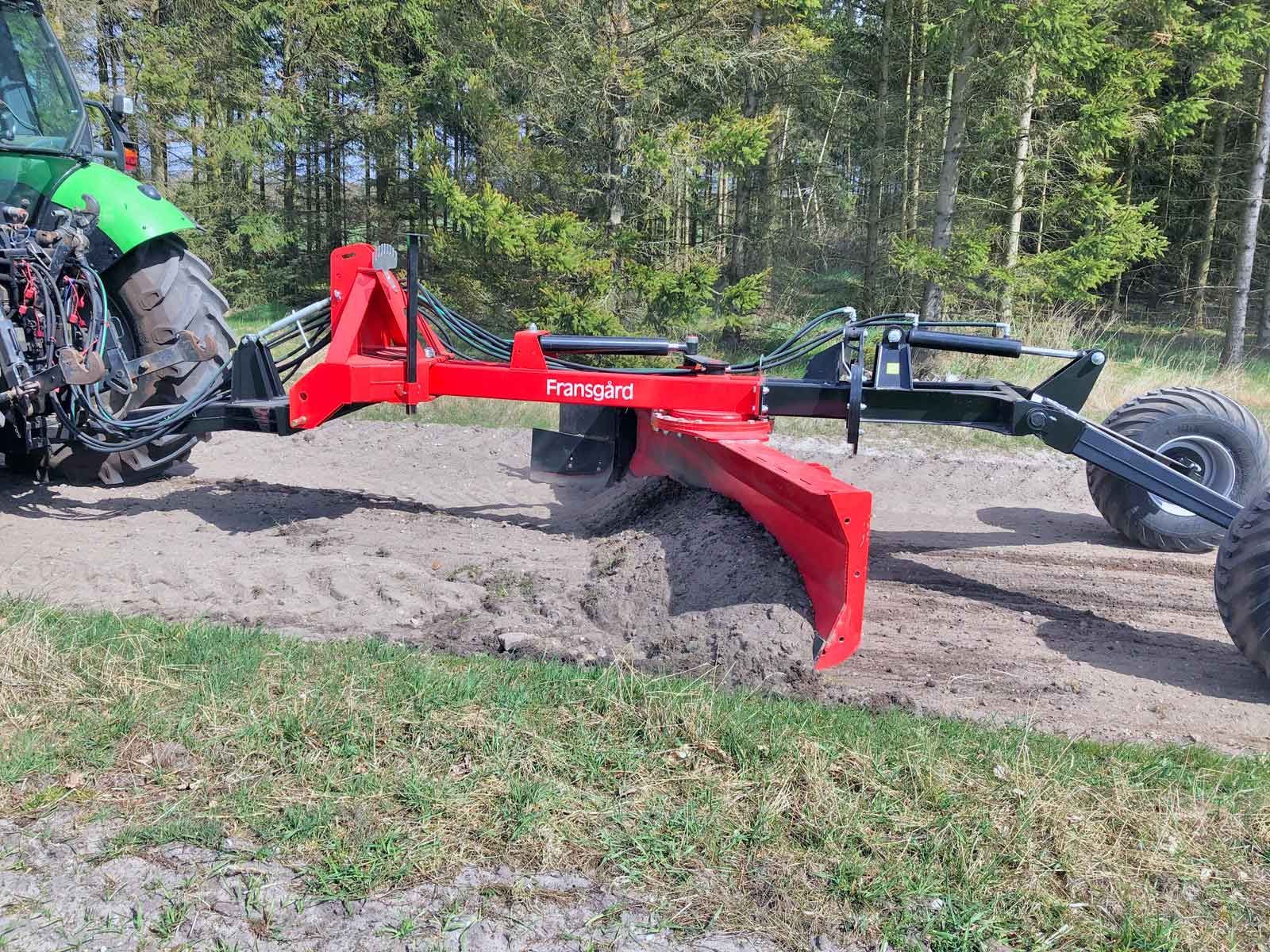 Ein rot-schwarzer Traktor steht am Rand einer unbefestigten Straße.