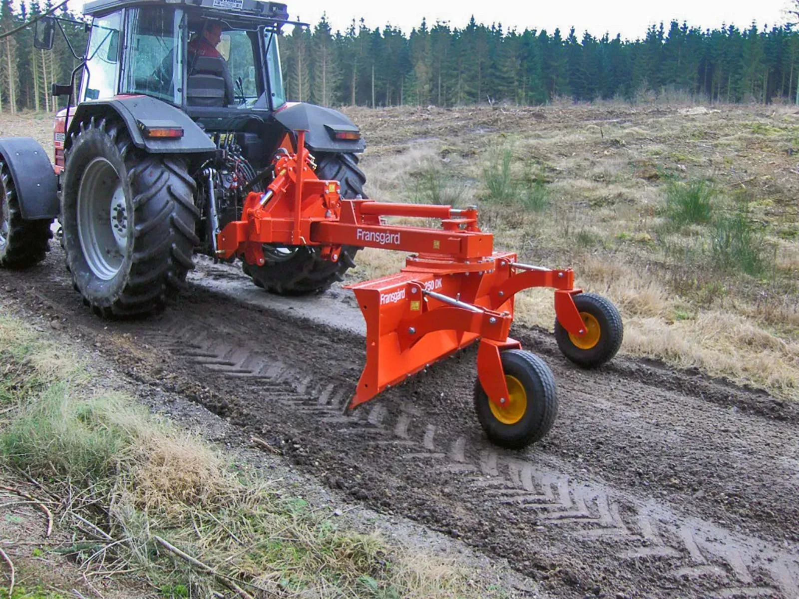Ein großer orangefarbener Traktor fährt eine unbefestigte Straße entlang