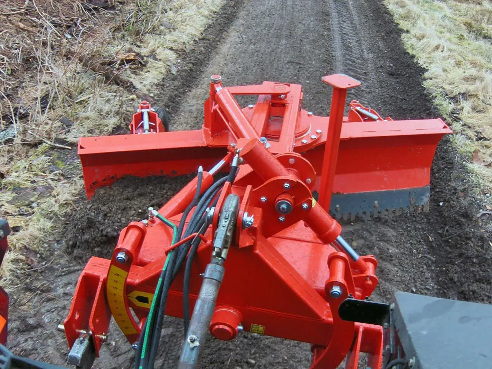 Ein roter Traktor fährt eine unbefestigte Straße entlang