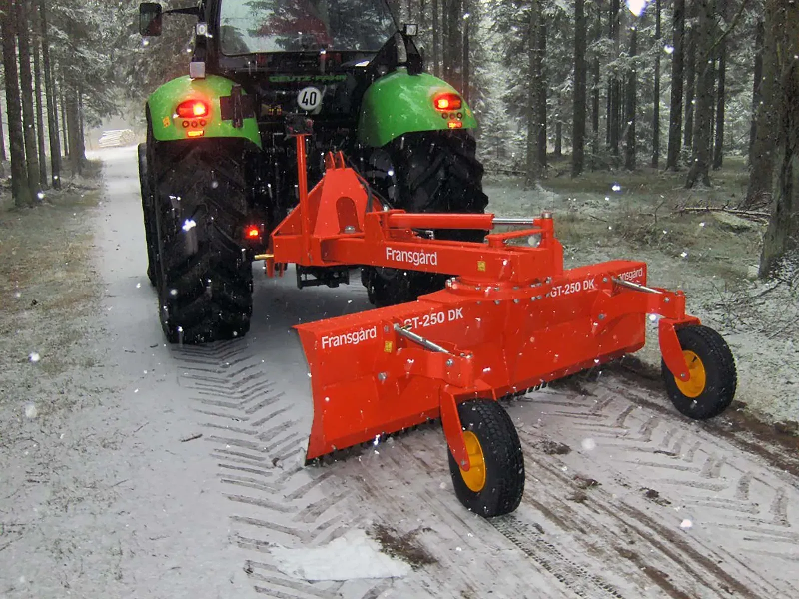 Ein grün-orangefarbener Traktor fährt eine verschneite Straße entlang
