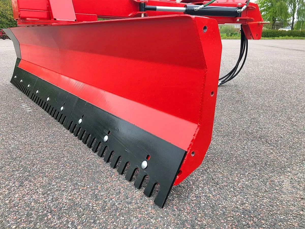 Ein rot-schwarzer Schneepflug steht auf einer Schotterstraße.