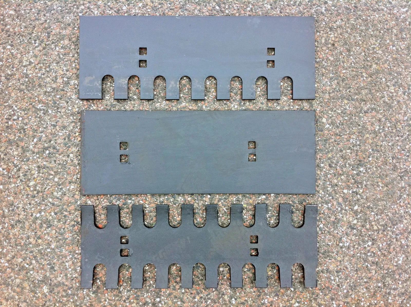 Zwei Metallstücke mit Löchern darin auf einer Kiesfläche