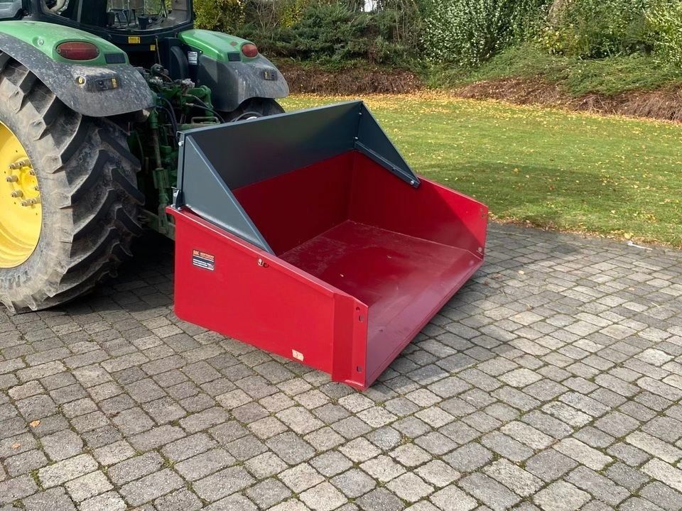 Auf einer gepflasterten Auffahrt steht ein Traktor mit einer daran befestigten roten Schaufel.