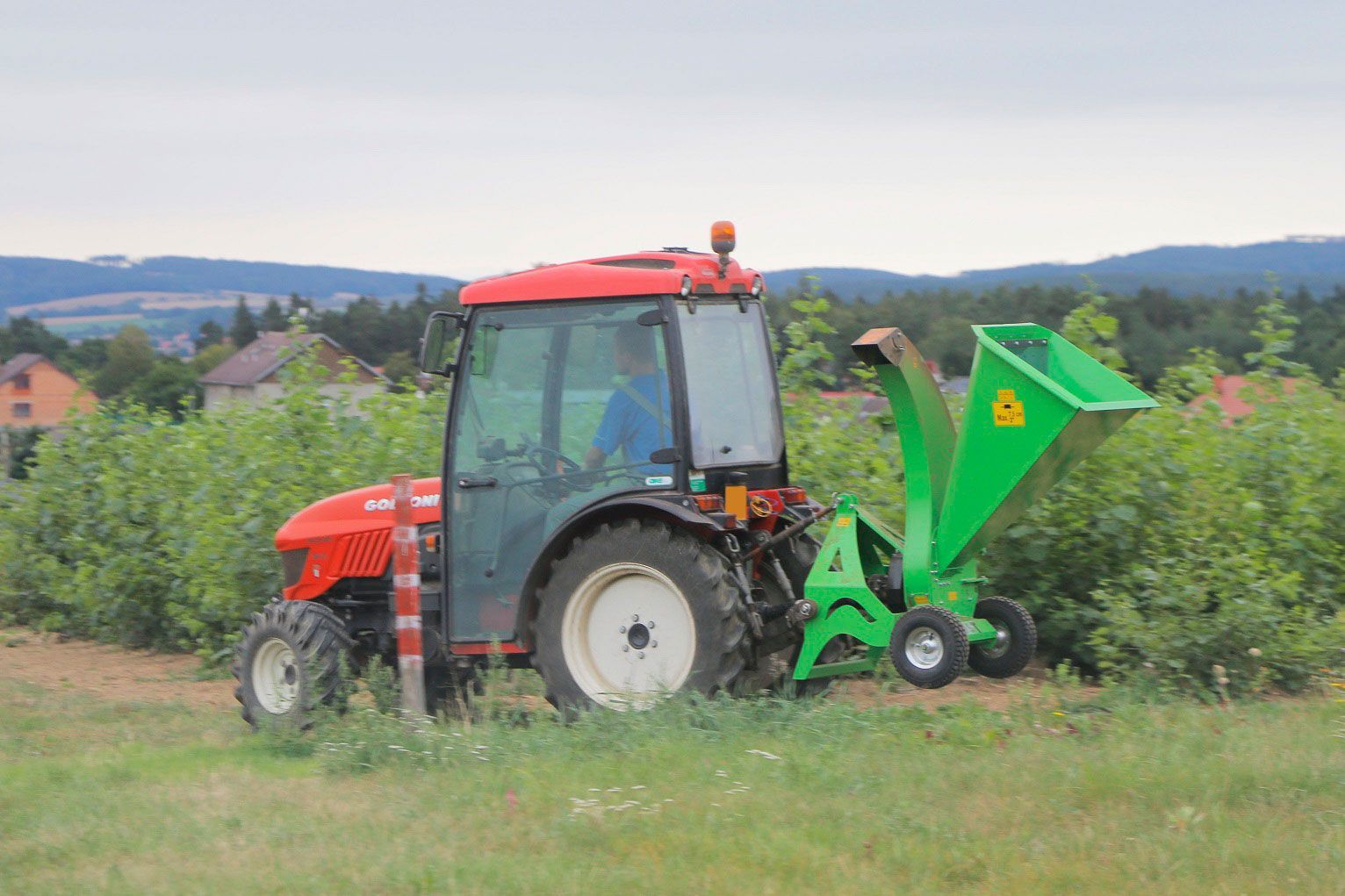Ein roter Traktor mit einem daran montierten grünen Häcksler fährt durch ein Feld.