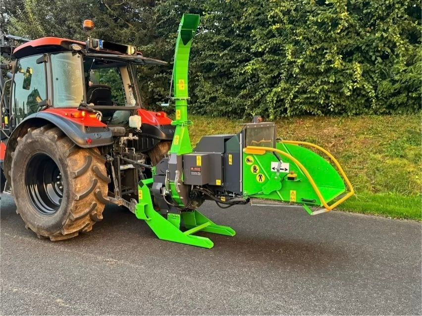 Am Straßenrand parkt ein Traktor mit einem daran befestigten Grünhäcksler.