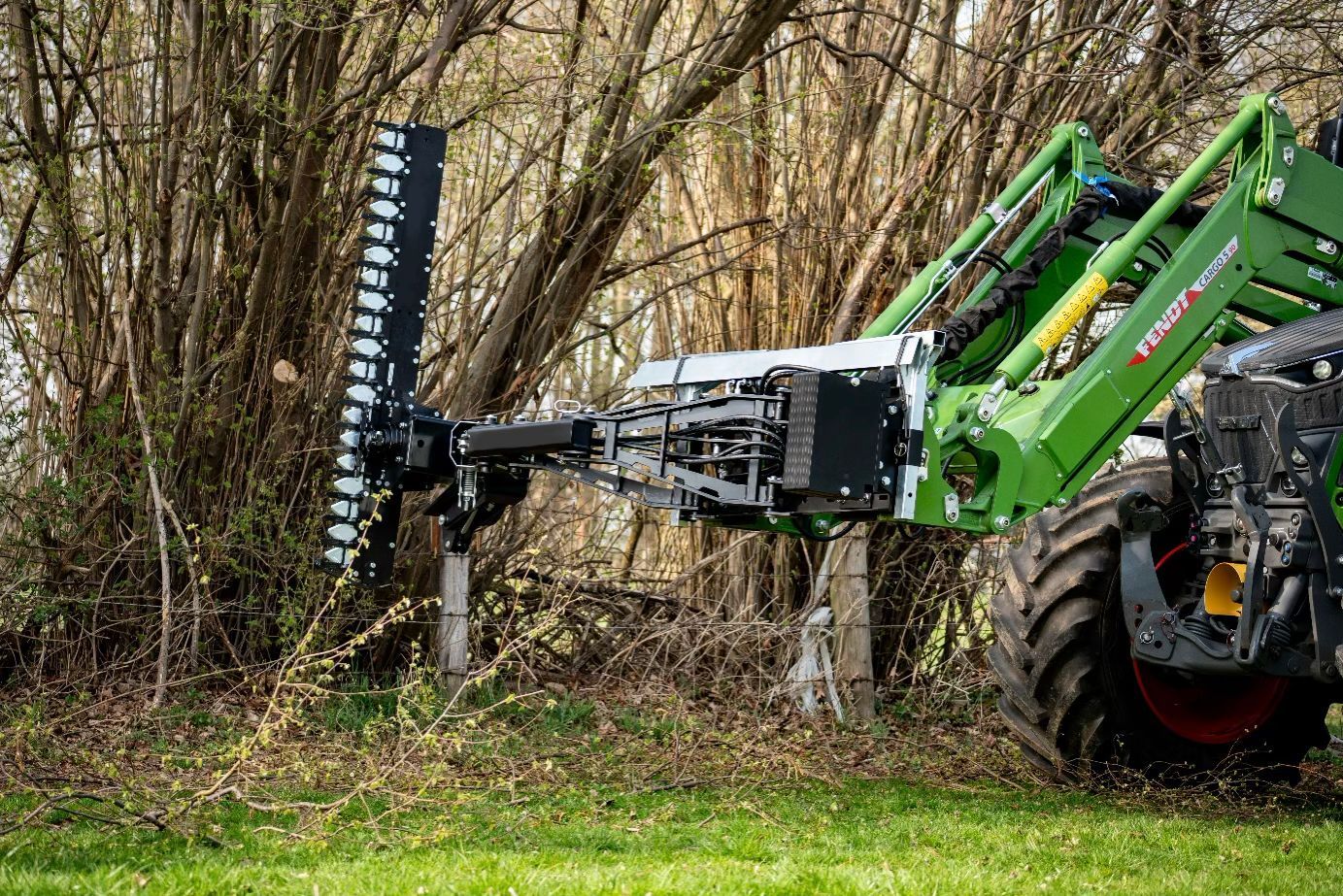 Ein Traktor mit angebauter Heckenschere schneidet eine Reihe Büsche auf einem Feld.