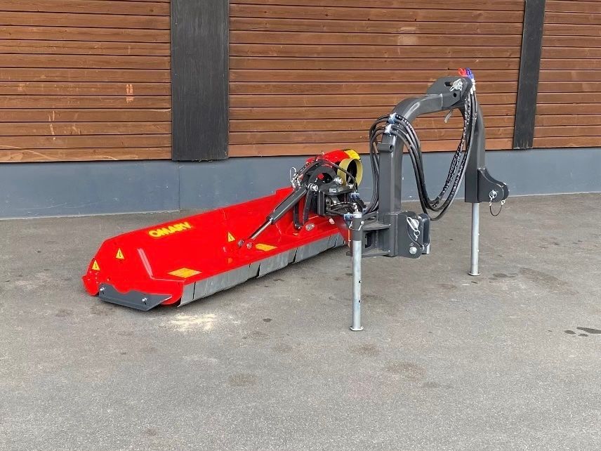 Eine rot-graue Maschine steht vor einem Holzgebäude.