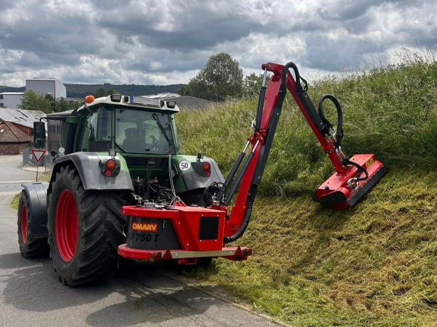 Ein Traktor mit einer daran befestigten Maschine mäht einen grasbewachsenen Hang.