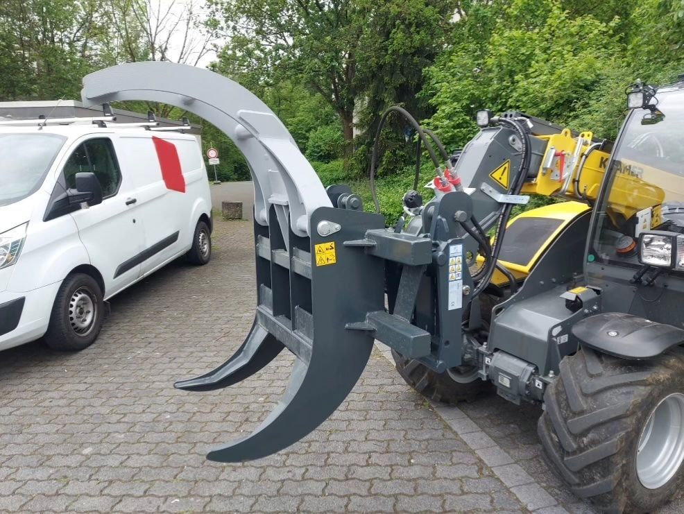 Ein Traktor mit einer großen Klaue daran ist neben einem weißen Lieferwagen geparkt.