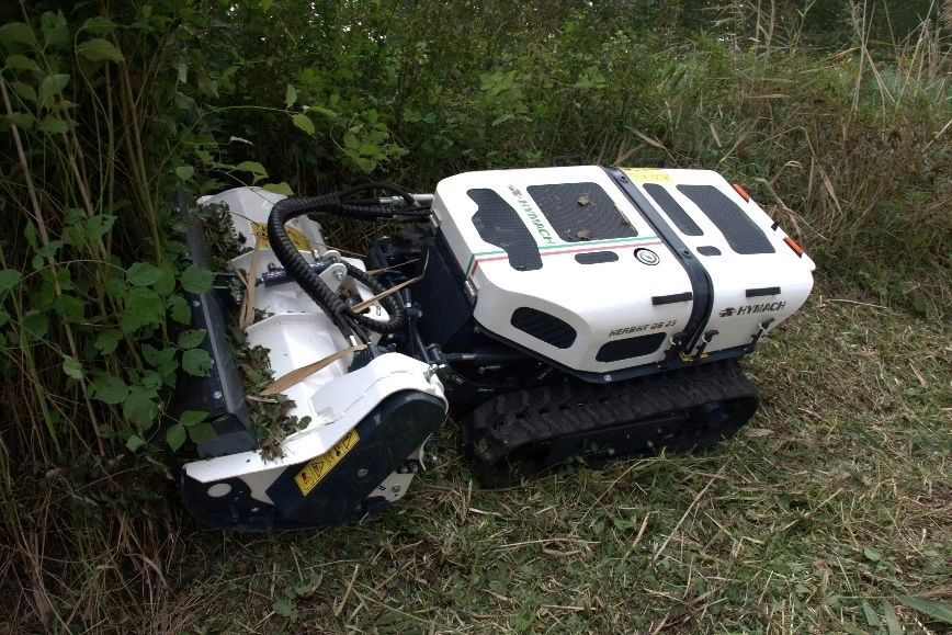 Ein weißer Traktor steht im Gras neben einem Busch.