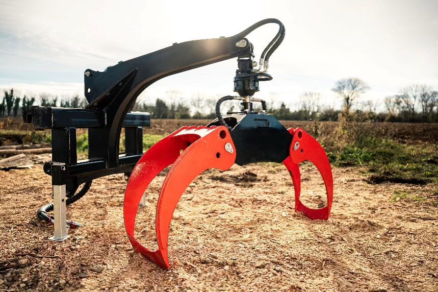 Ein roter und schwarzer Greifarm hebt Baumstämme auf einem sonnigen Feld an.