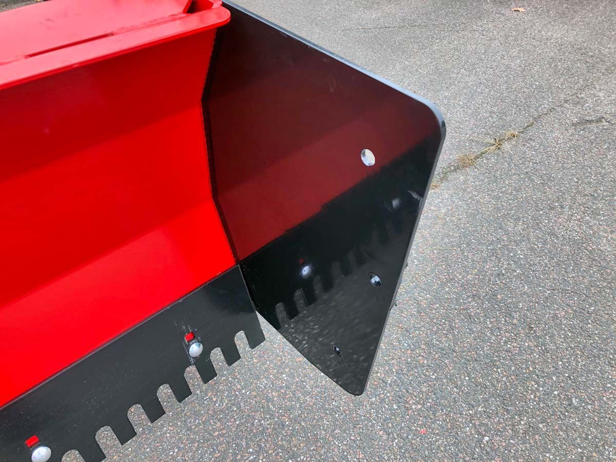 Auf dem Boden steht ein rot-schwarzer Eimer mit einer schwarzen Schaufel.