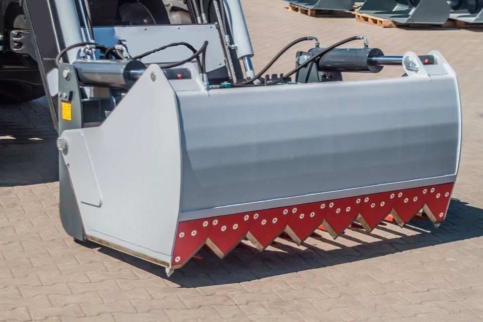 Neben einem Traktor steht ein großer Eimer auf dem Boden.