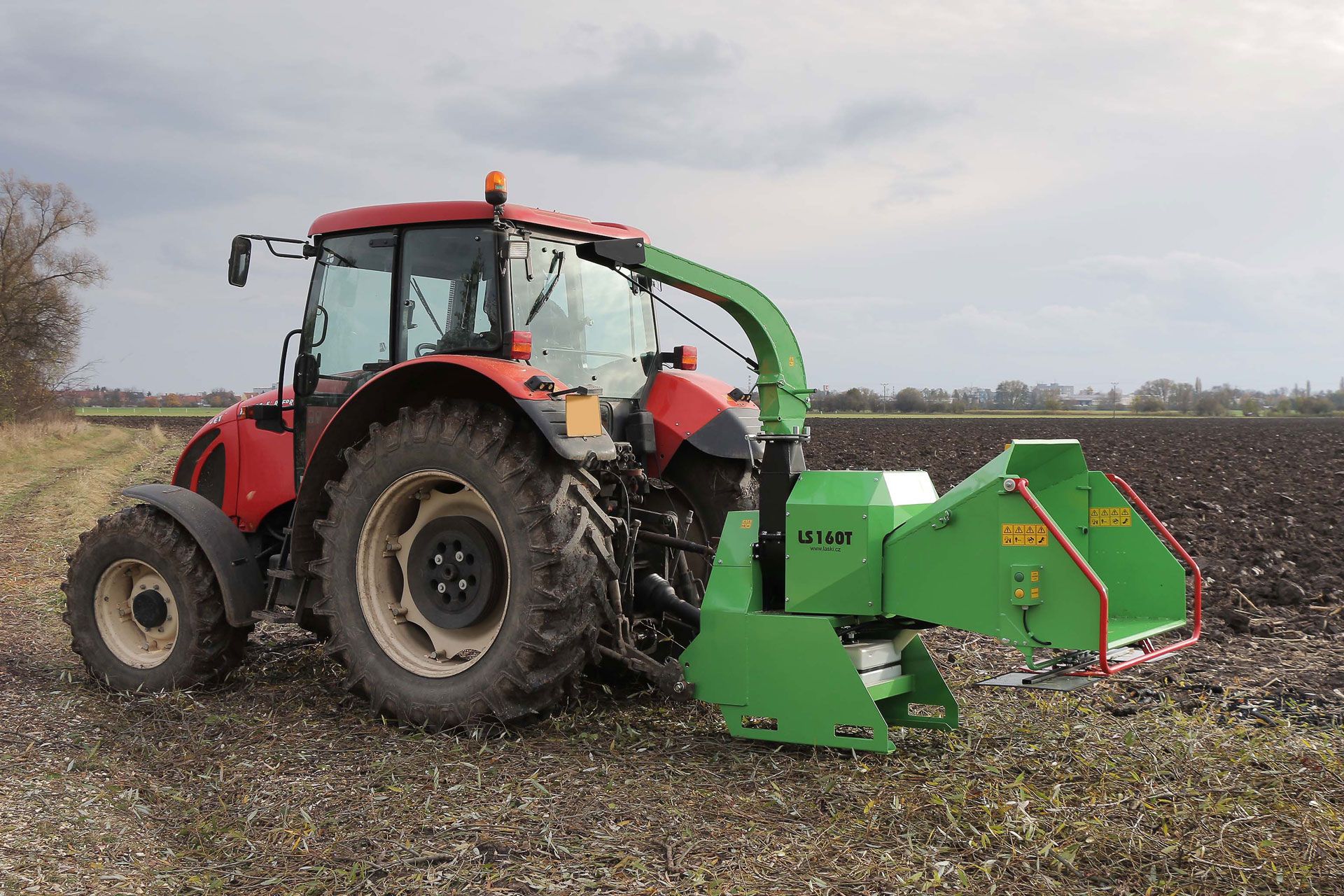 Ein roter Traktor mit einem daran montierten grünen Häcksler steht auf einem Feld.