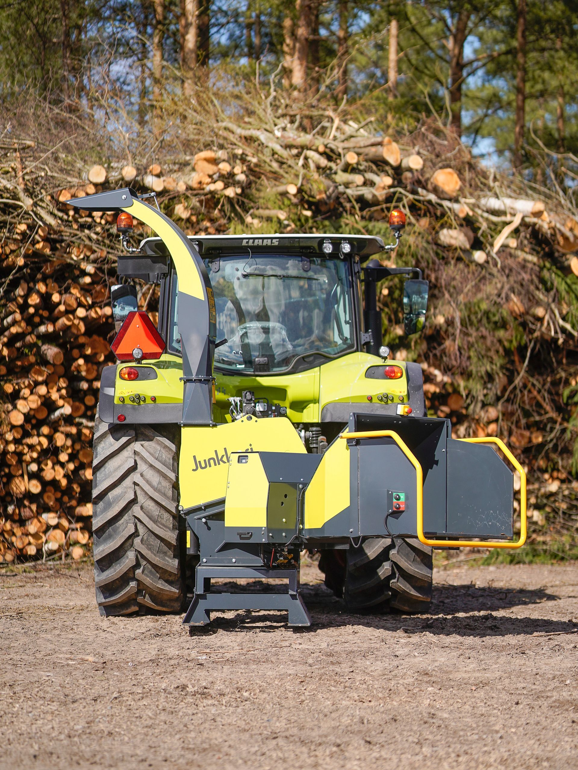 Ein gelb-schwarzer Traktor steht vor einem Stapel Baumstämme.