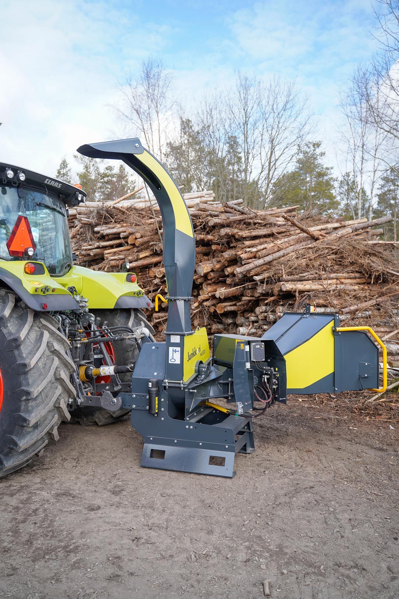 Vor einem Stapel Baumstämme steht ein Traktor.